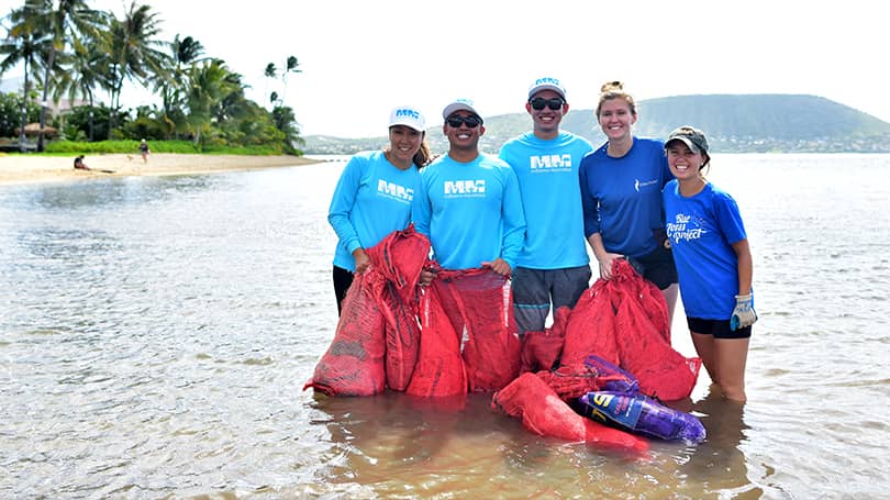 Five volunteers in the ocean shore picking up trash